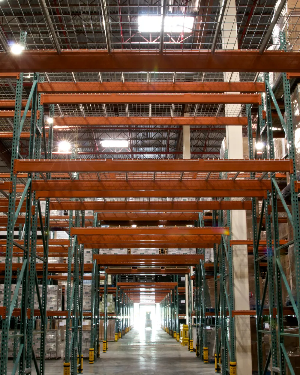 Long warehouse aisle between steel pallet racks stacked with shrink-wrapped cartons